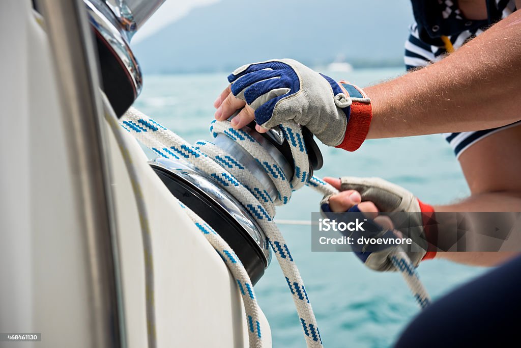 Hands operating a sailboat winch while wearing protective gloves
